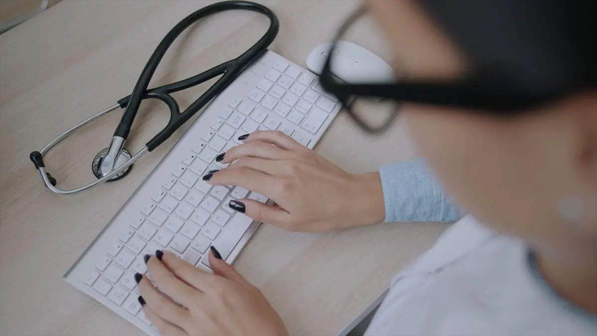 Médica escribiendo en el teclado de su computadora, con el estetoscopio sobre el escritorio