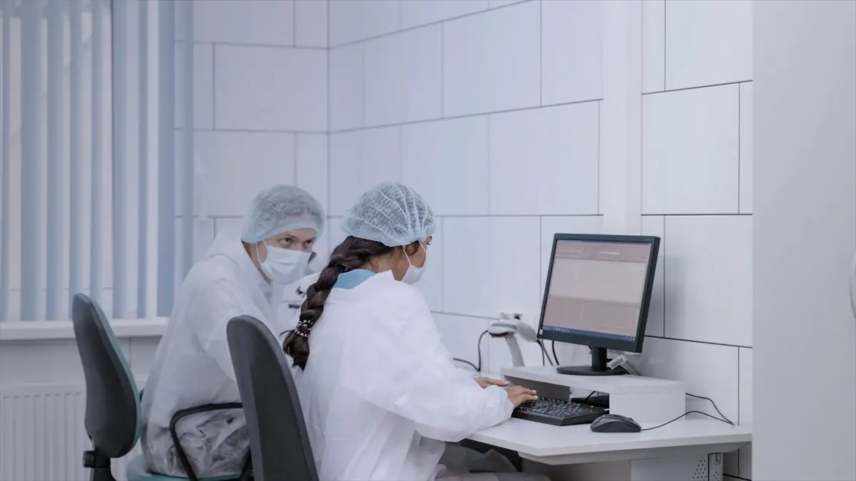 Dos profesionales de laboratorio con cofia y tapabocas trabajando frente a una computadora