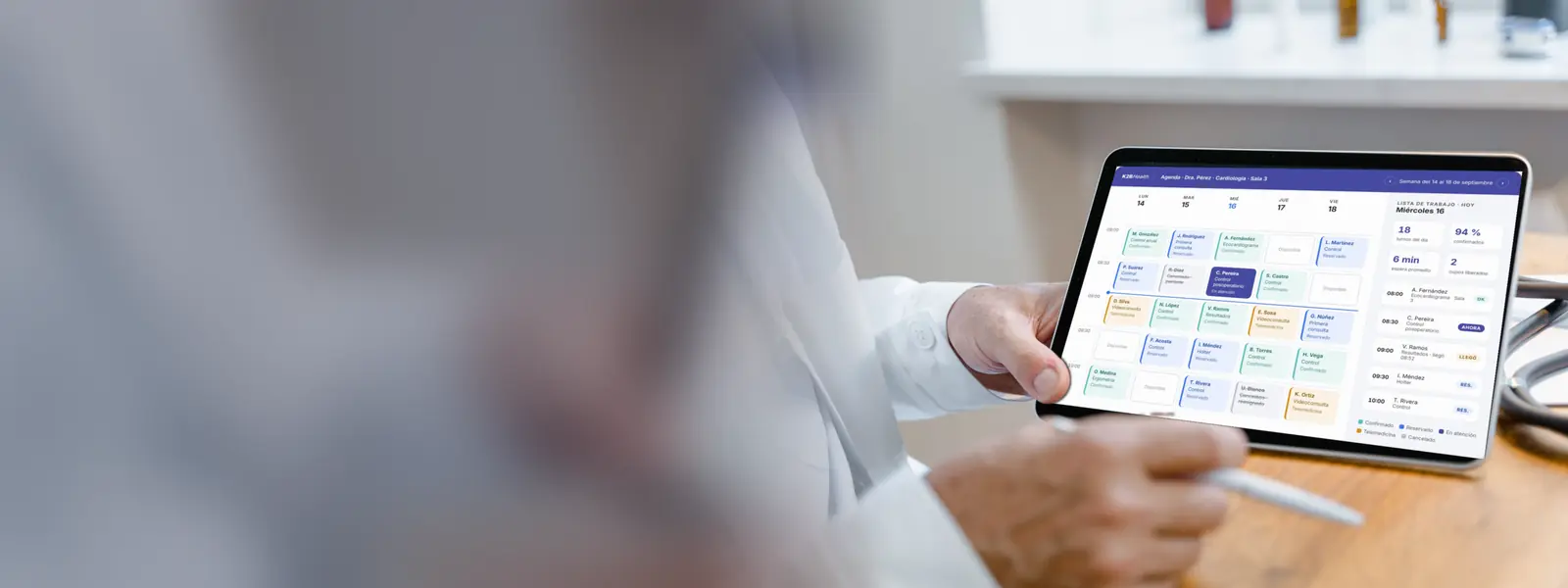 Médico con túnica blanca sosteniendo en su consultorio una tableta con la agenda de K2BHealth