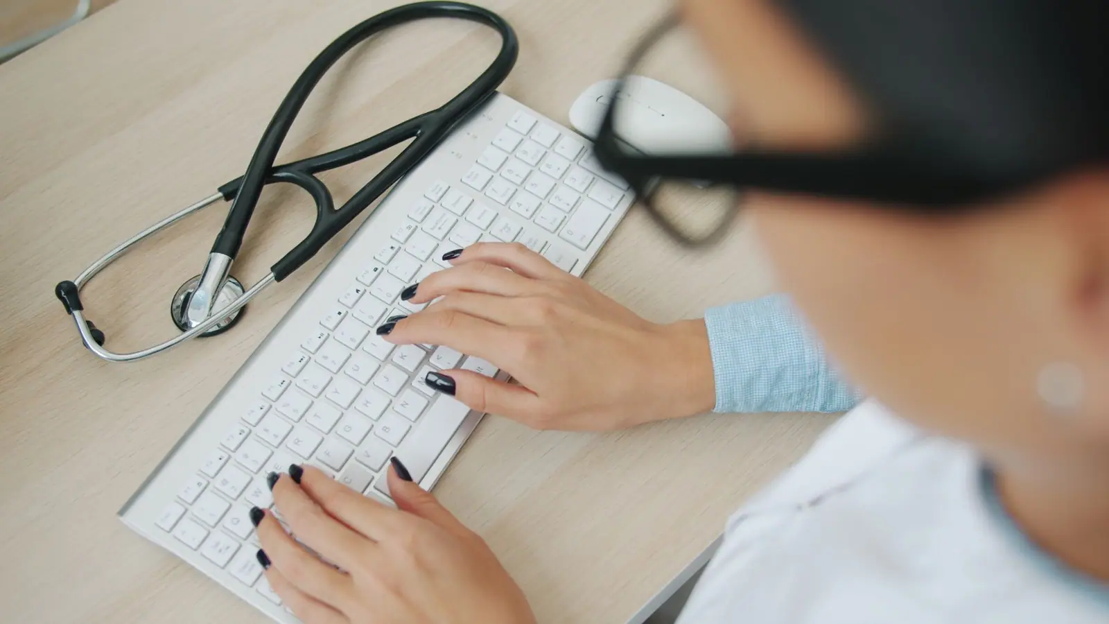 Profesional de la salud escribiendo en el teclado, con un estetoscopio sobre el escritorio